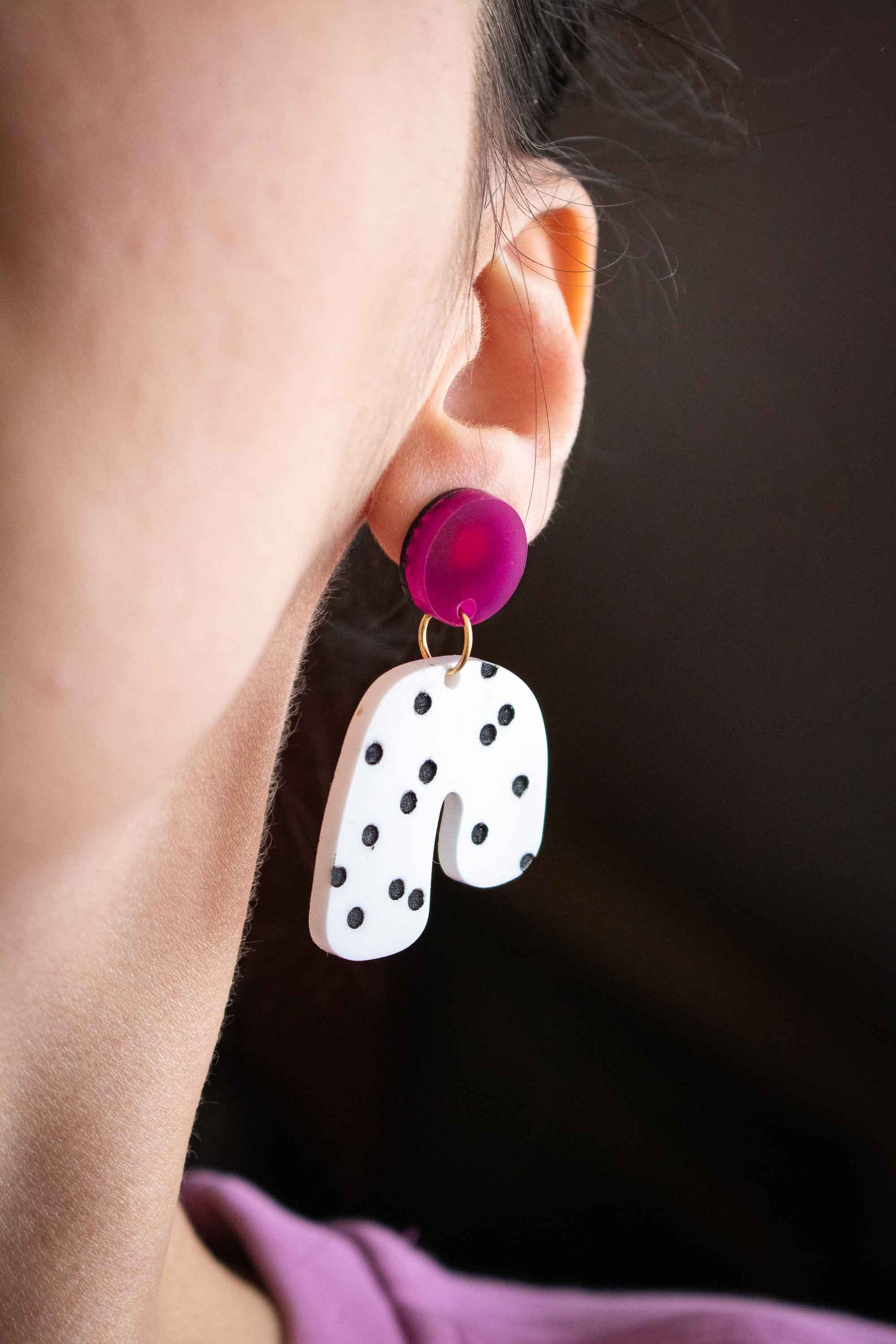 Gros plan boucles d'oreilles acrylique rose et blanc à pois noirs portées sur oreille, Limonade Studio