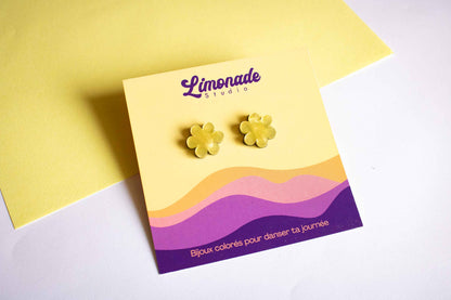 Boucles d'oreilles puces fleur jaune en acrylique découpé au laser, présentées sur leur carte d'emballage Limonade Studio, fond jaune