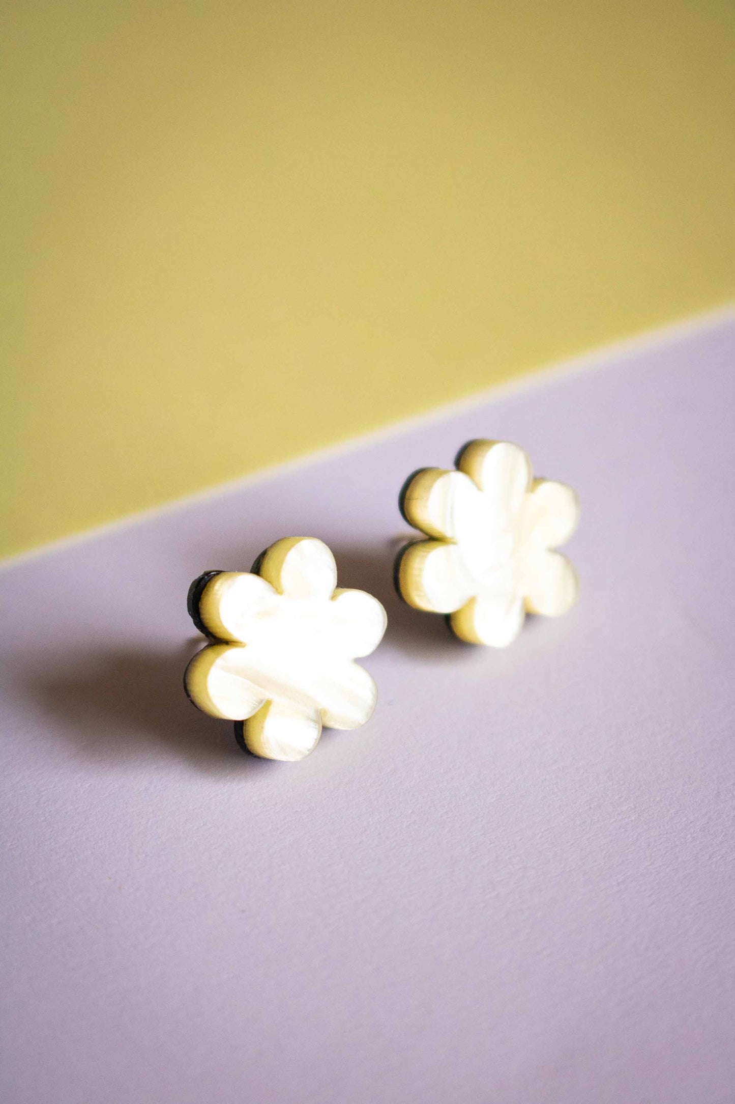 Boucles d'oreilles puces fleur jaune acrylique posées sur fond bicolore jaune et violet, bijoux faits main Limonade Studio