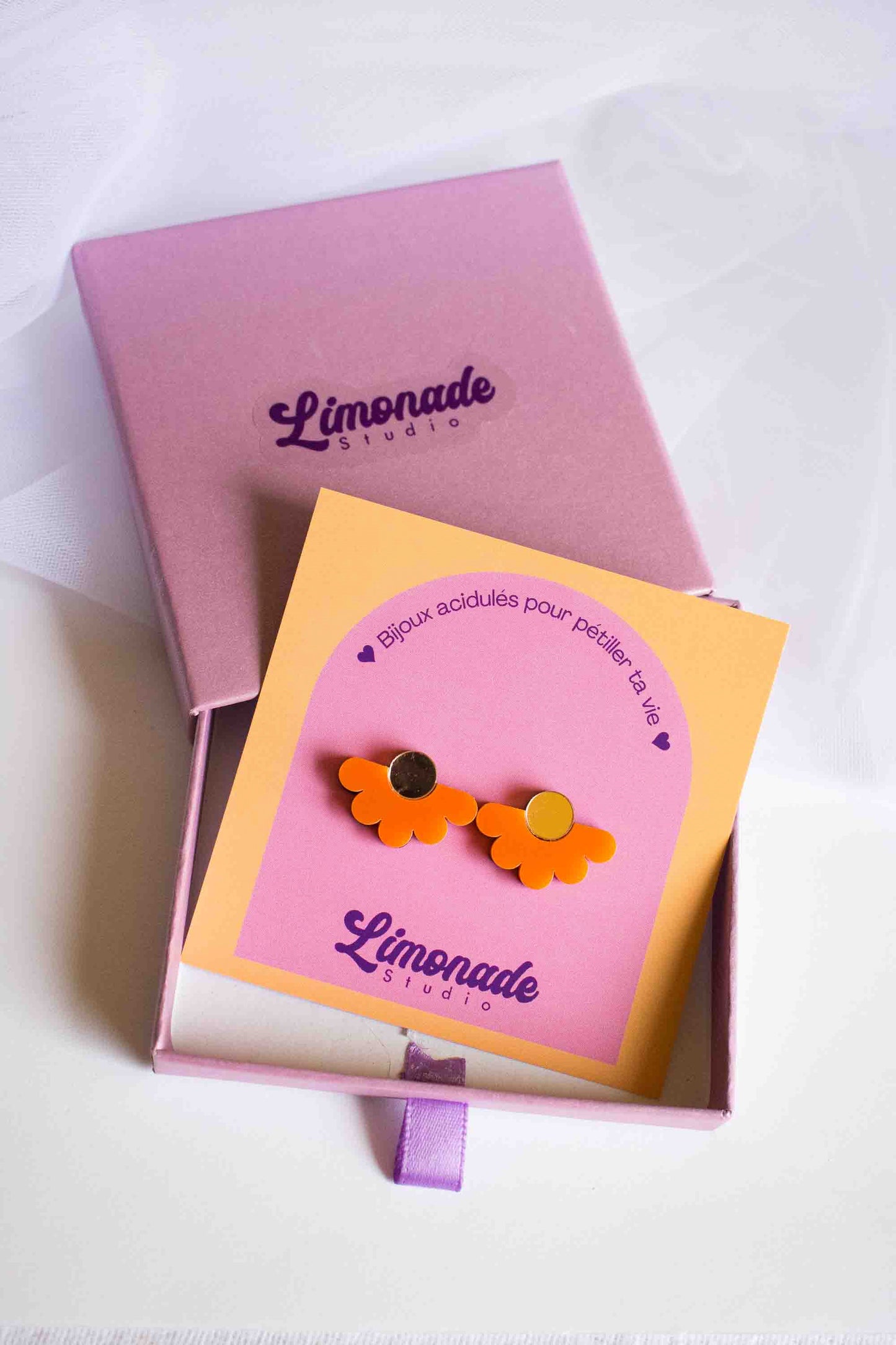Boucles d'oreilles puces fleur orange en acrylique découpé au laser, présentées sur cartonnette Limonade Studio dans leur boîte cadeau rose, vue de dessus
