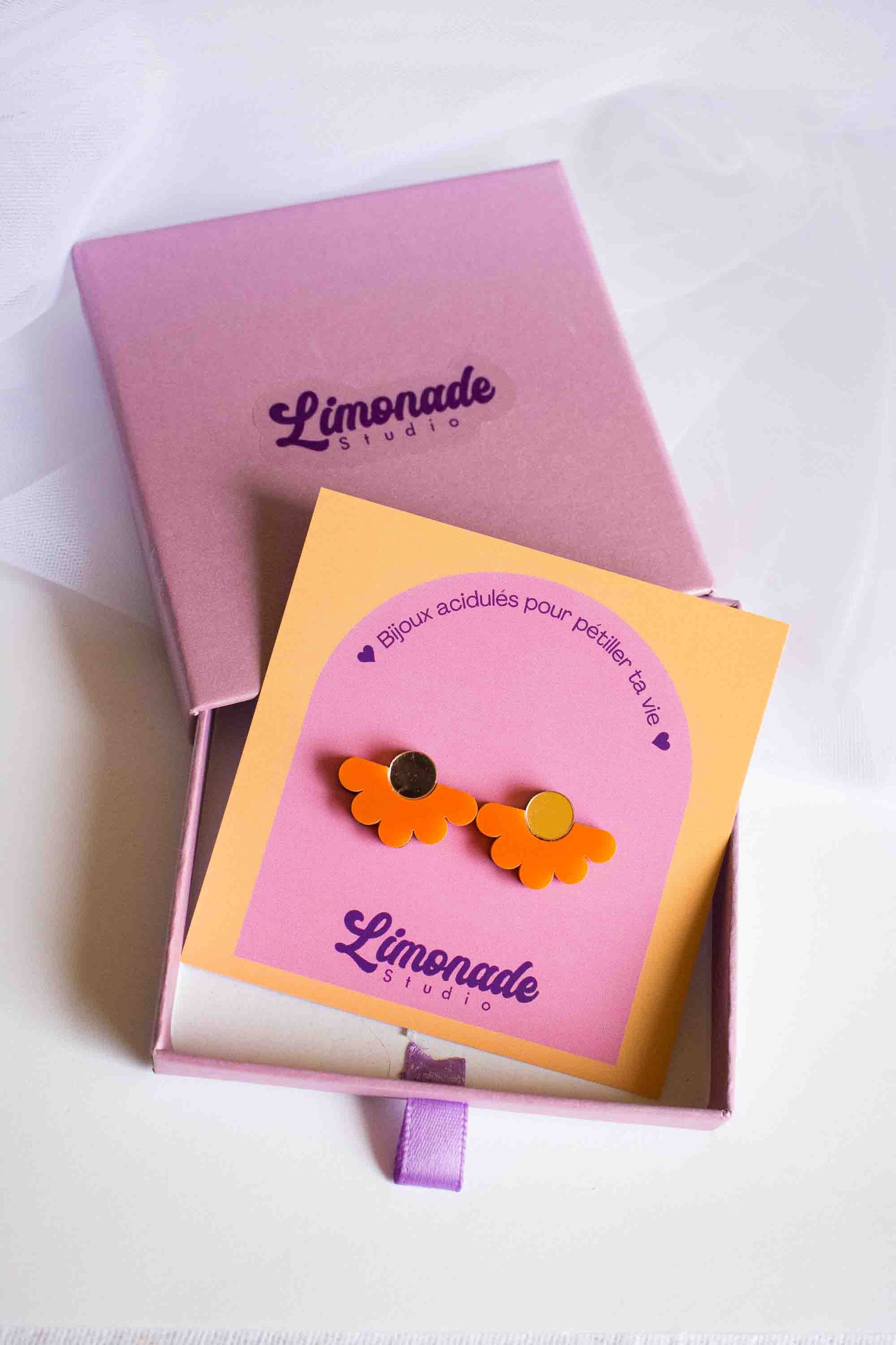 Boucles d'oreilles puces fleur orange en acrylique découpé au laser, présentées sur cartonnette Limonade Studio dans leur boîte cadeau rose, vue de dessus
