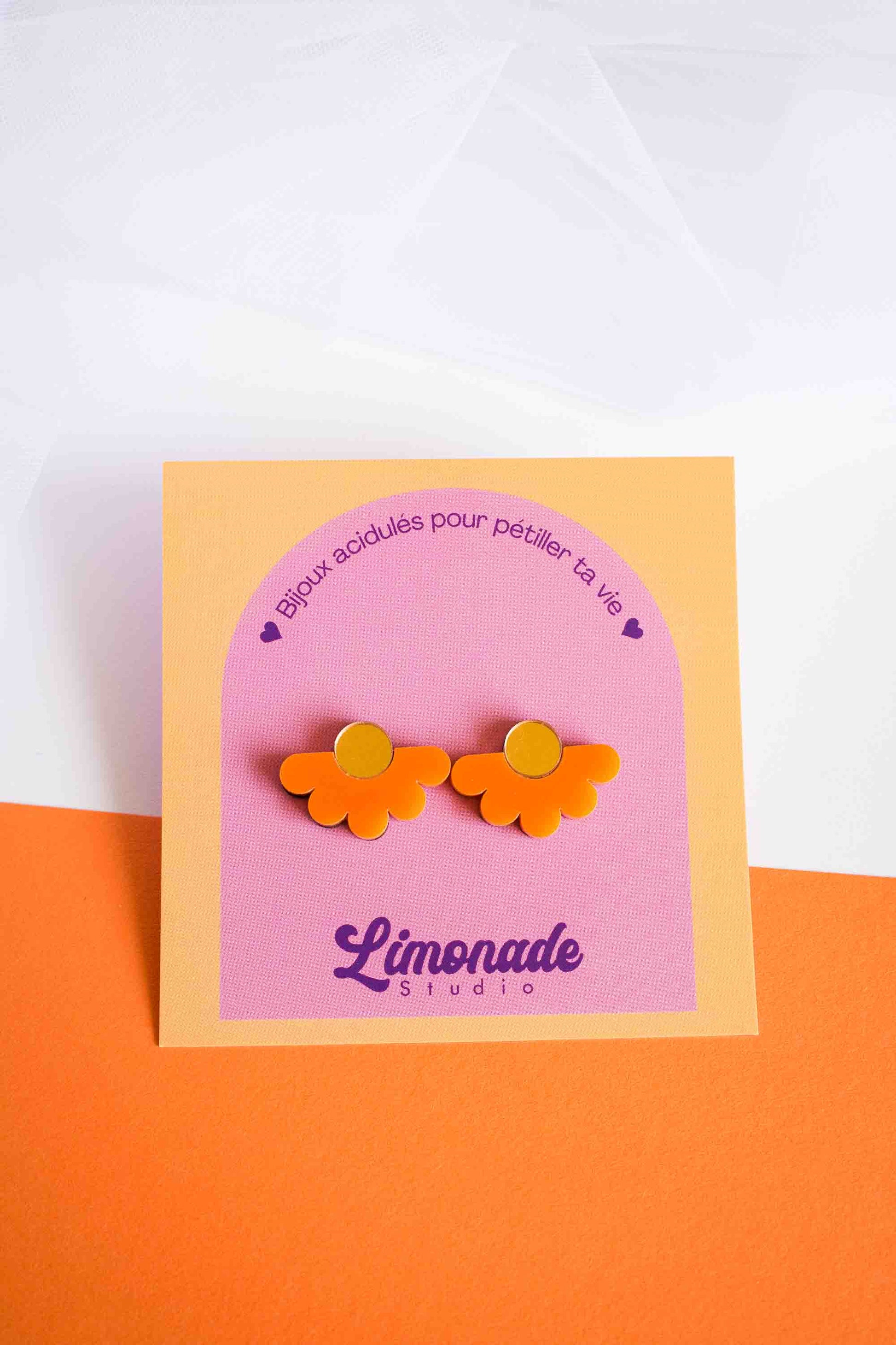 Puces fleur orange en acrylique découpé au laser sur cartonnette Limonade Studio, fond bicolore blanc et orange, cadrage serré