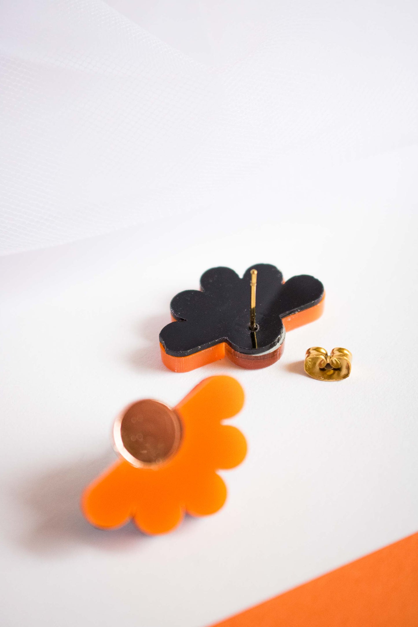Détail du dos des puces fleur orange acrylique, fond noir de découpe laser, tige et poussette dorées en acier inoxydable