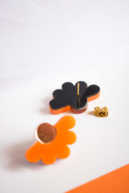 Détail du dos des puces fleur orange acrylique, fond noir de découpe laser, tige et poussette dorées en acier inoxydable