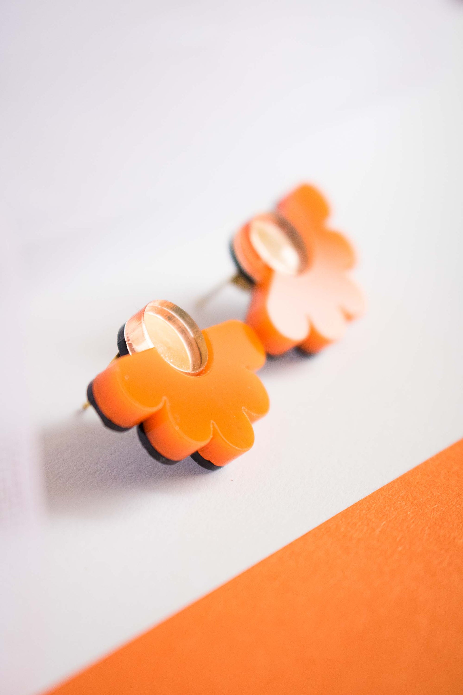 Gros plan sur les puces fleur orange en acrylique découpé au laser, centre miroir doré, texture et reflets, sur cartonnette Limonade Studio