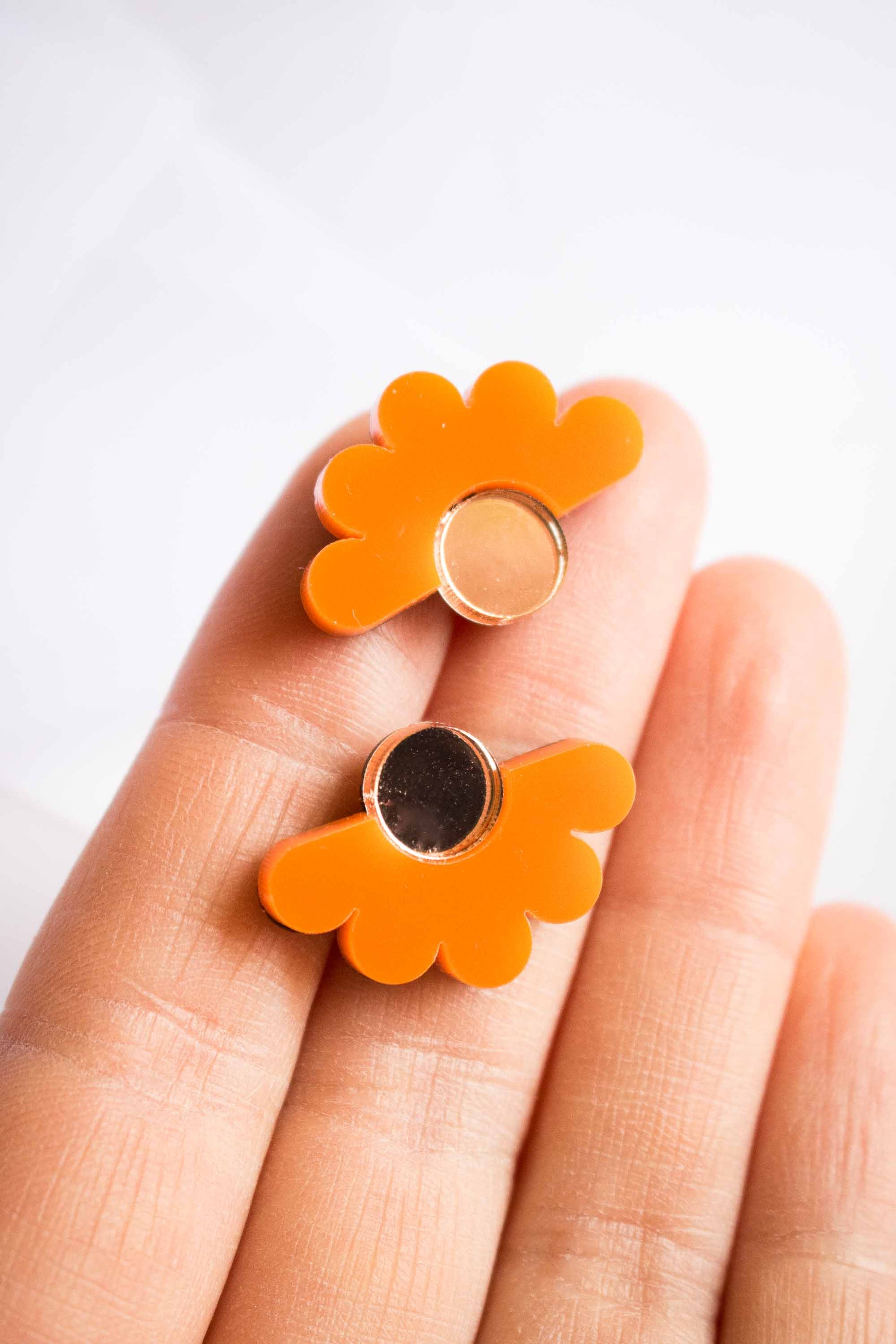 Puces fleur orange en acrylique découpé au laser tenues dans la paume, centre miroir doré, bijoux faits main Limonade Studio