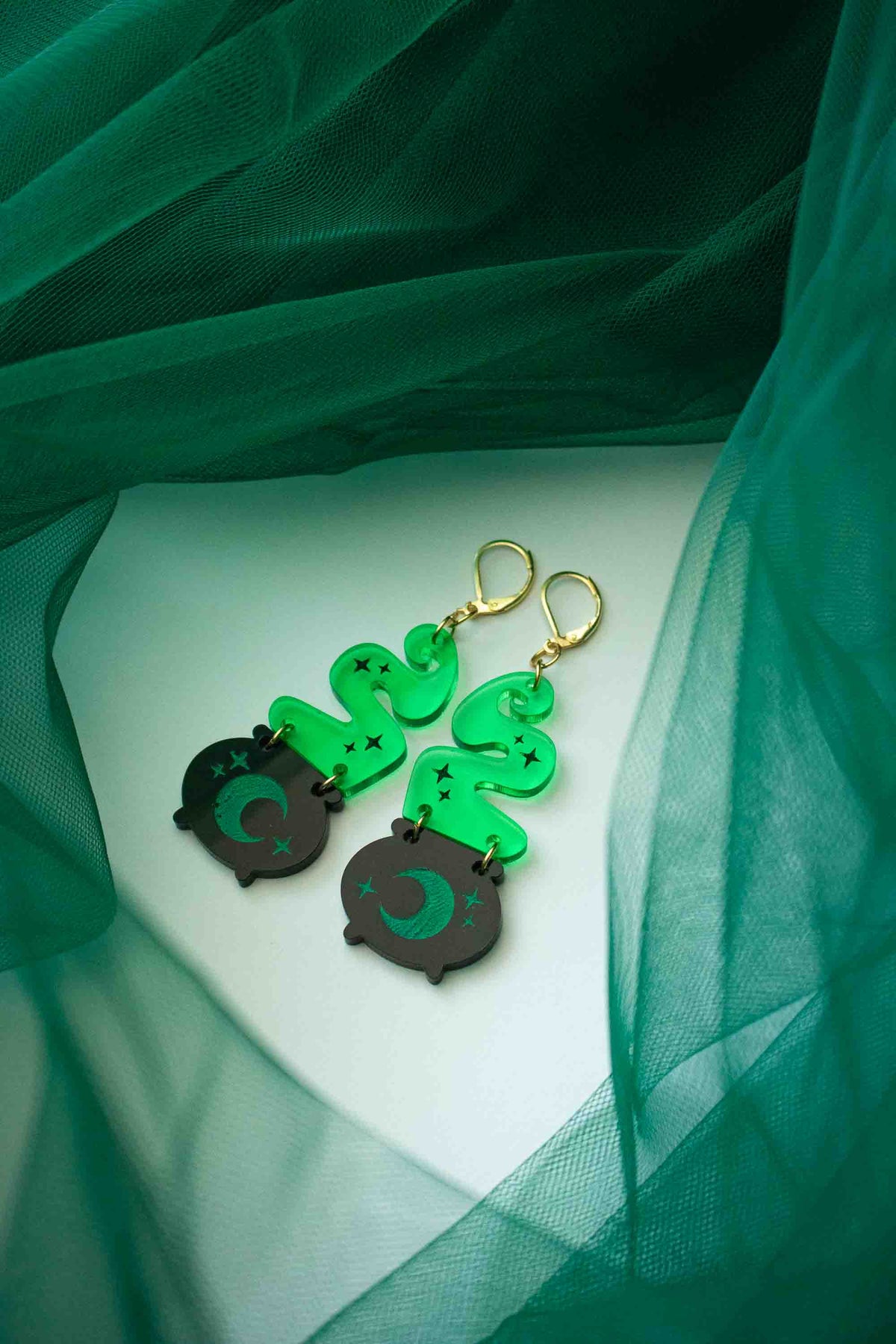 Boucles d’oreilles de sorcière chaudron noir photographiées sur un fond vert drapé