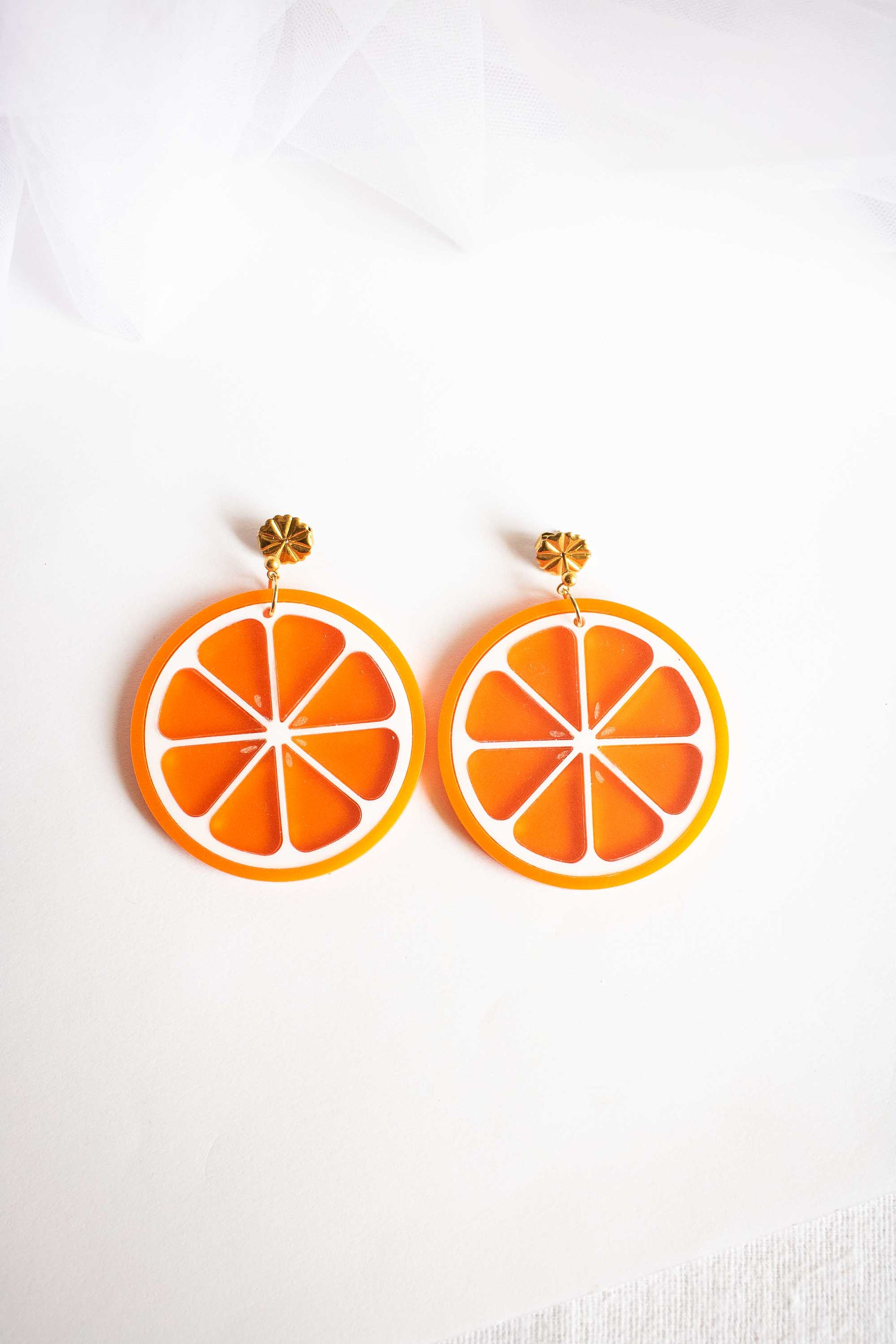 Boucles d'oreilles pendantes tranche d'orange acidulé en acrylique découpé au laser, puce dorée, fait main par Limonade Studio, posées sur fond blanc