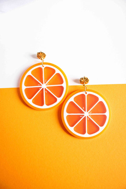 Boucles d'oreilles tranche d'orange bijou coloré fait main en acrylique, puce dorée, Limonade Studio, posées sur fond bicolore blanc et orange vif