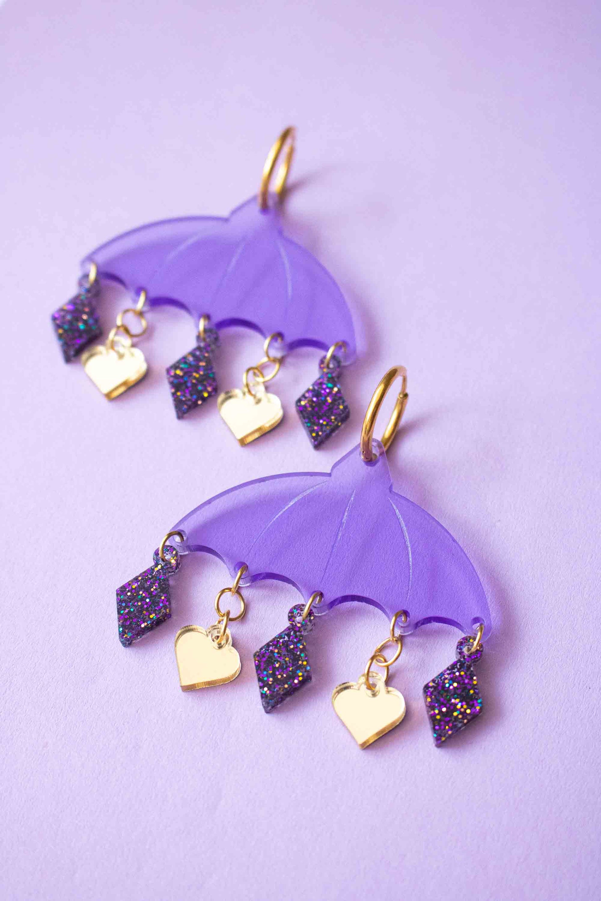 Boucles d'oreilles violettes en acrylique decoupe laser, bijou colore artisanal Limonade Studio, deux paires posees sur fond lilas lumineux.