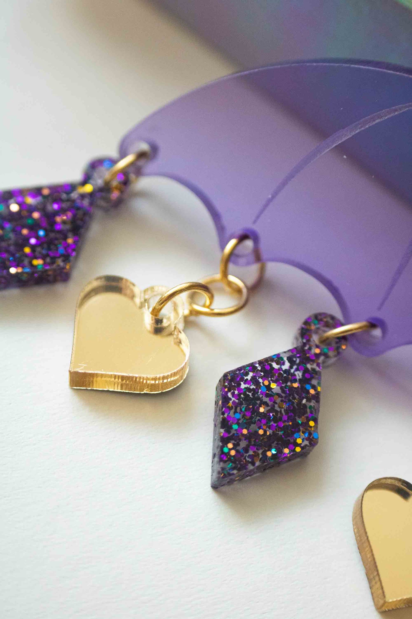 Boucles d'oreilles violettes en acrylique decoupe laser, bijou colore fait main Limonade Studio, gros plan sur les charms pailletes sur fond blanc.