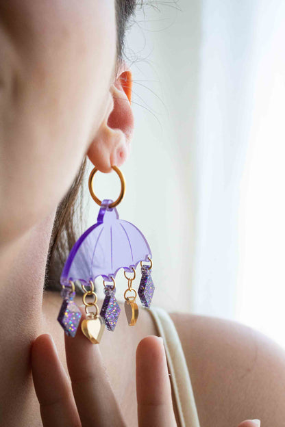 Boucles d'oreilles violettes en acrylique decoupe laser, bijou colore artisanal Limonade Studio, portees a l oreille en portrait sur fond clair.