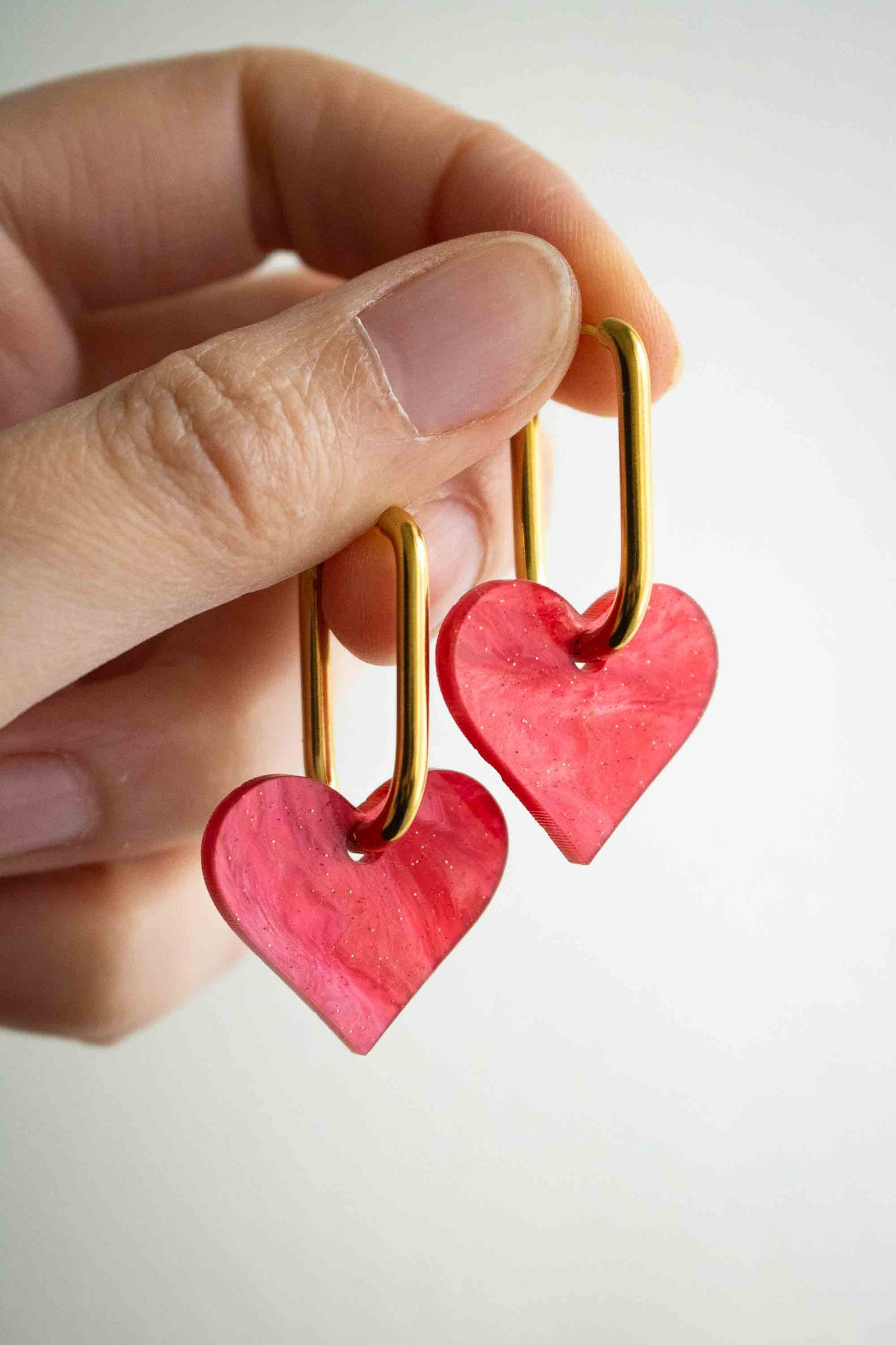 Paire de boucles pendantes cœur rouge acrylique pailleté tenue en main, cadeau femme original fait main par Limonade Studio, fond blanc