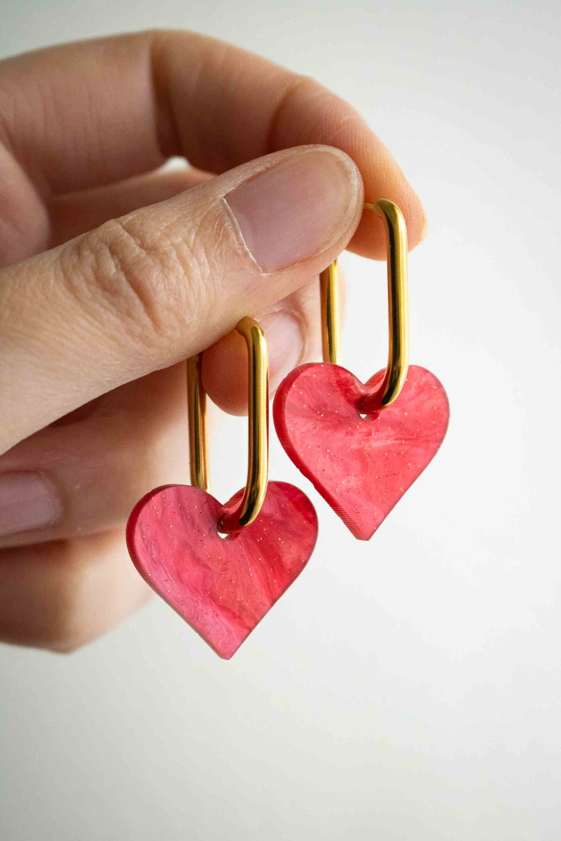 Paire de boucles pendantes cœur rouge acrylique pailleté tenue en main, cadeau femme original fait main par Limonade Studio, fond blanc