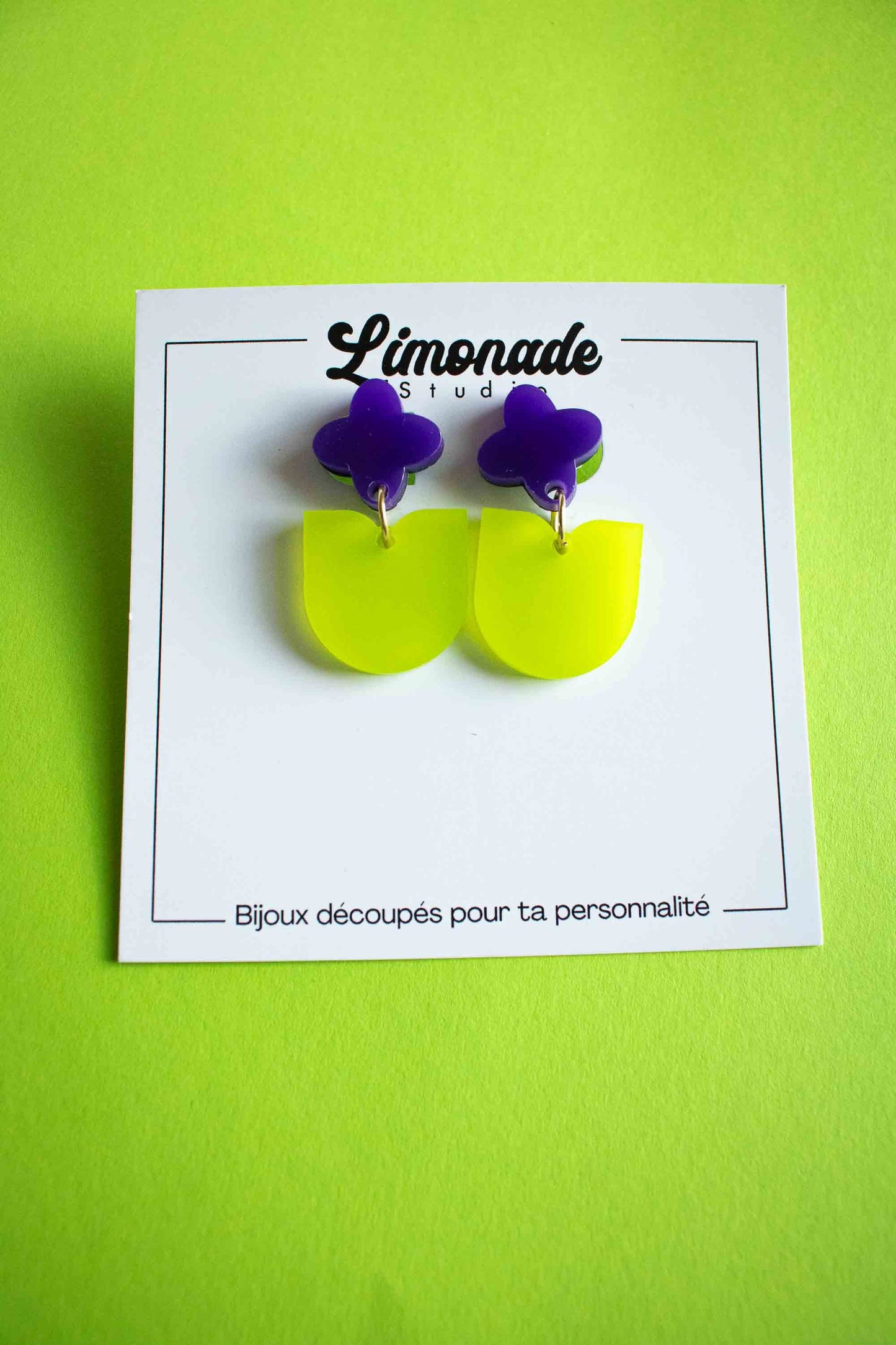 Boucles d'oreilles fantaisie fleur violette pendante verte acrylique, cadeau femme artisanal Limonade Studio, vue face sur cartonnette