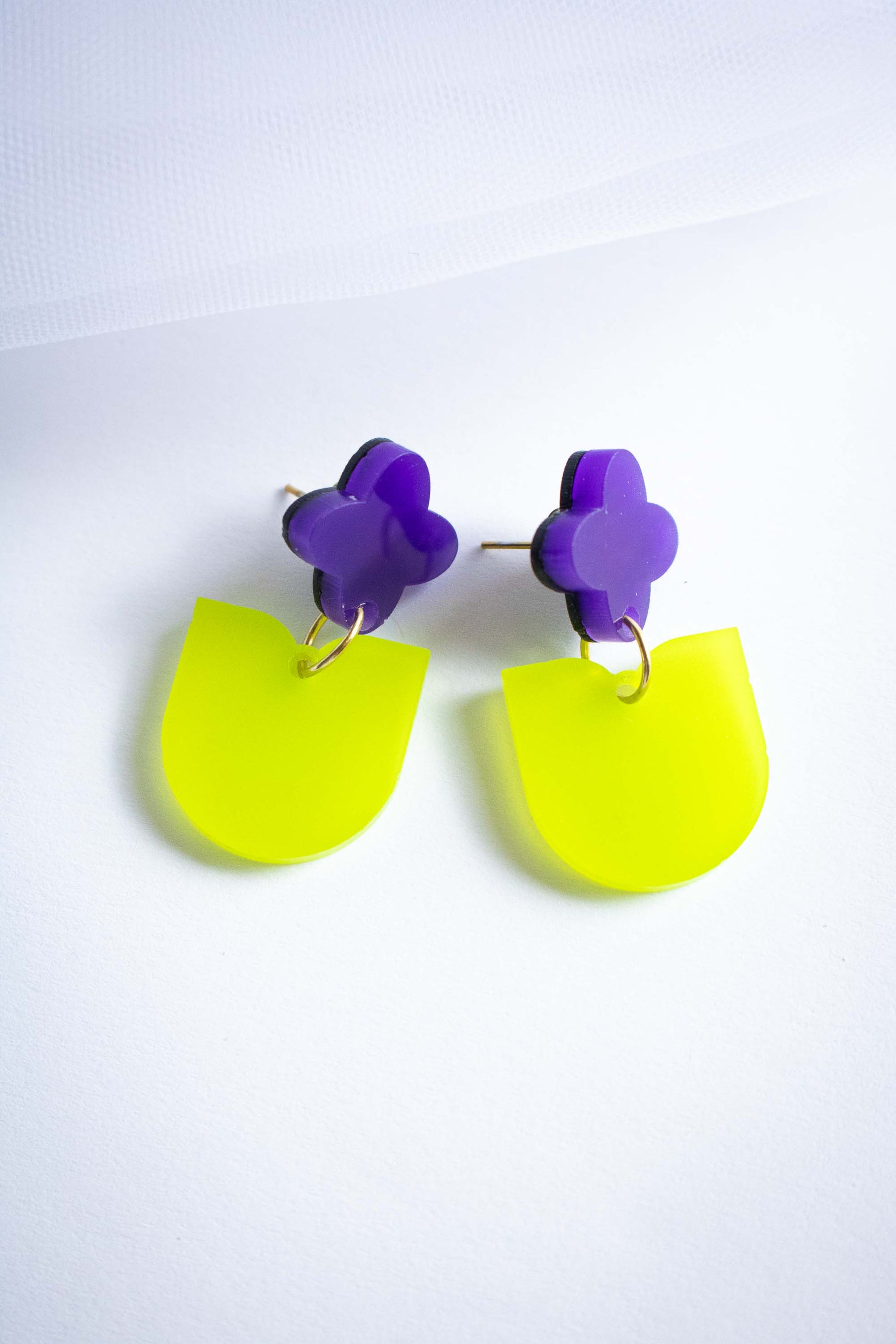 Boucles pendantes fleur violette pendante verte acrylique dépoli, bijou coloré fait main Limonade Studio, posées à plat fond blanc