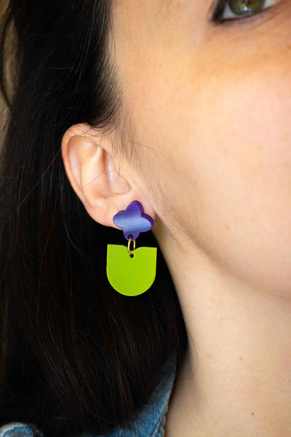 Gros plan sur boucles pendantes fleur violette et feuille verte acrylique dépoli, découpe laser artisanale Limonade Studio, portées sur oreille