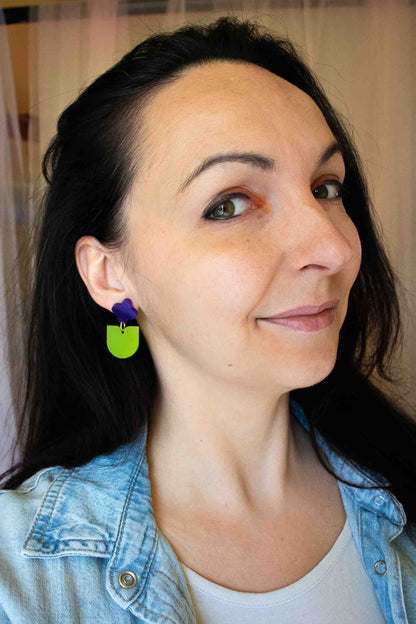 Boucles d'oreilles pendantes fleur violette et pendante verte en acrylique dépoli, fait main par Limonade Studio, portées par une femme