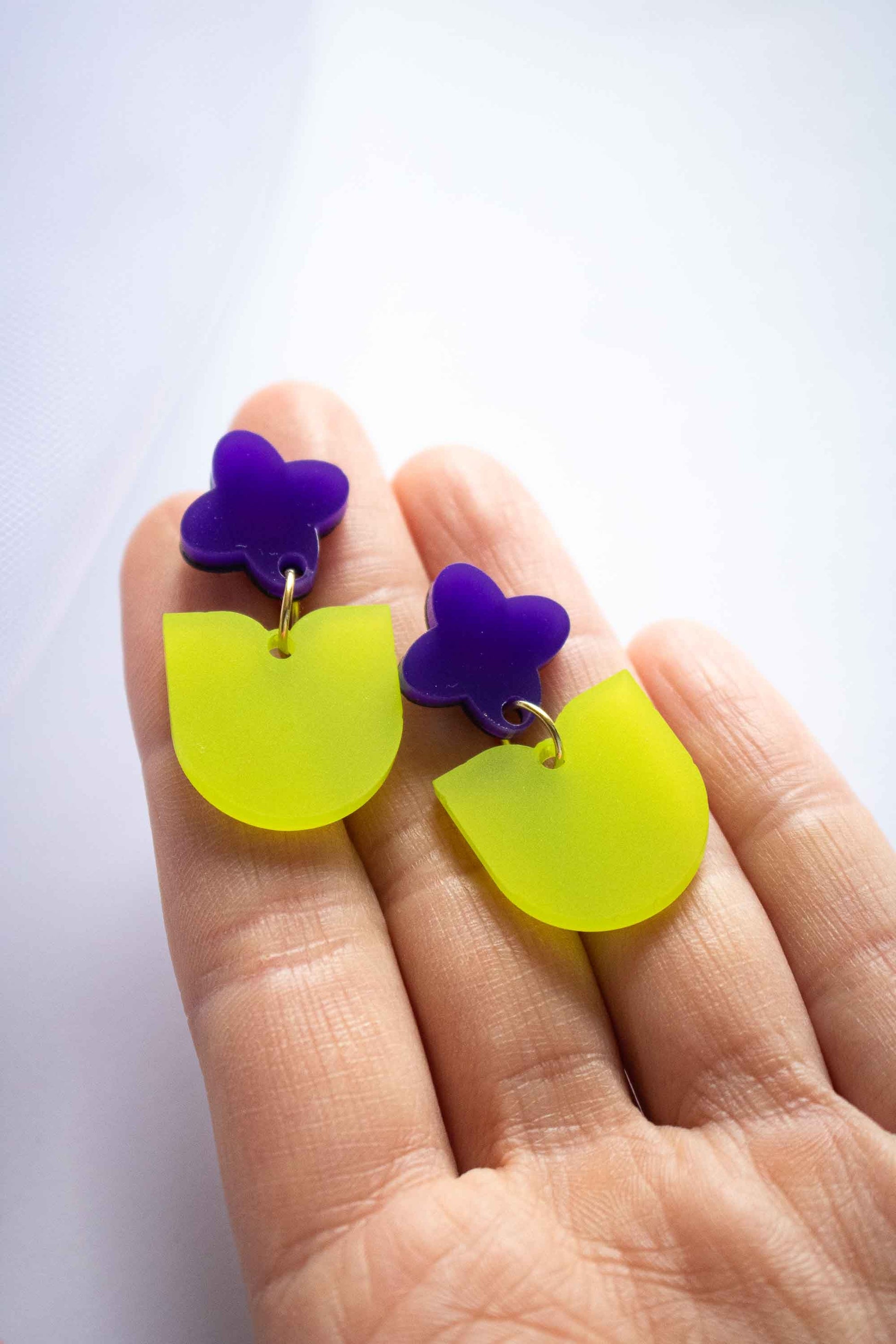 Boucles d'oreilles fantaisie fleur violette et feuille verte acrylique dépoli artisanal Limonade Studio, posées sur paume de main