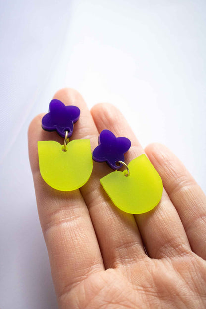 Boucles d'oreilles fantaisie fleur violette et feuille verte acrylique dépoli artisanal Limonade Studio, posées sur paume de main