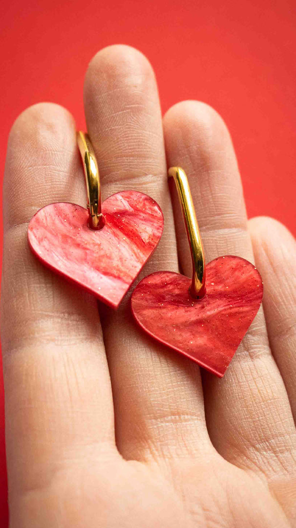 Vidéo des boucles pendantes cœur rouge acrylique marbré pailleté Limonade Studio, portées à l'oreille et présentées dans leur boîte cadeau violette, bijou fantaisie fait main découpé au laser