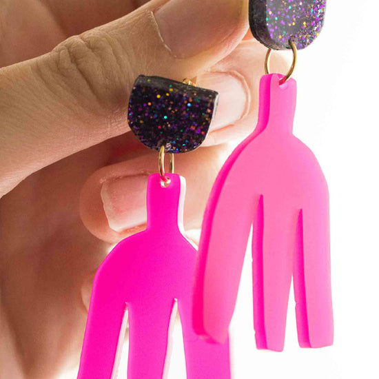 Vidéo des boucles d'oreilles pendantes rose fuchsia en acrylique découpé au laser Limonade Studio : clou pailleté holographique, vue portée puis présentées sur leur cartonnette d'emballage, bijoux faits main colorés