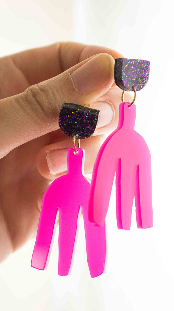 Vidéo des boucles d'oreilles pendantes rose fuchsia en acrylique découpé au laser Limonade Studio : clou pailleté holographique, vue portée puis présentées sur leur cartonnette d'emballage, bijoux faits main colorés