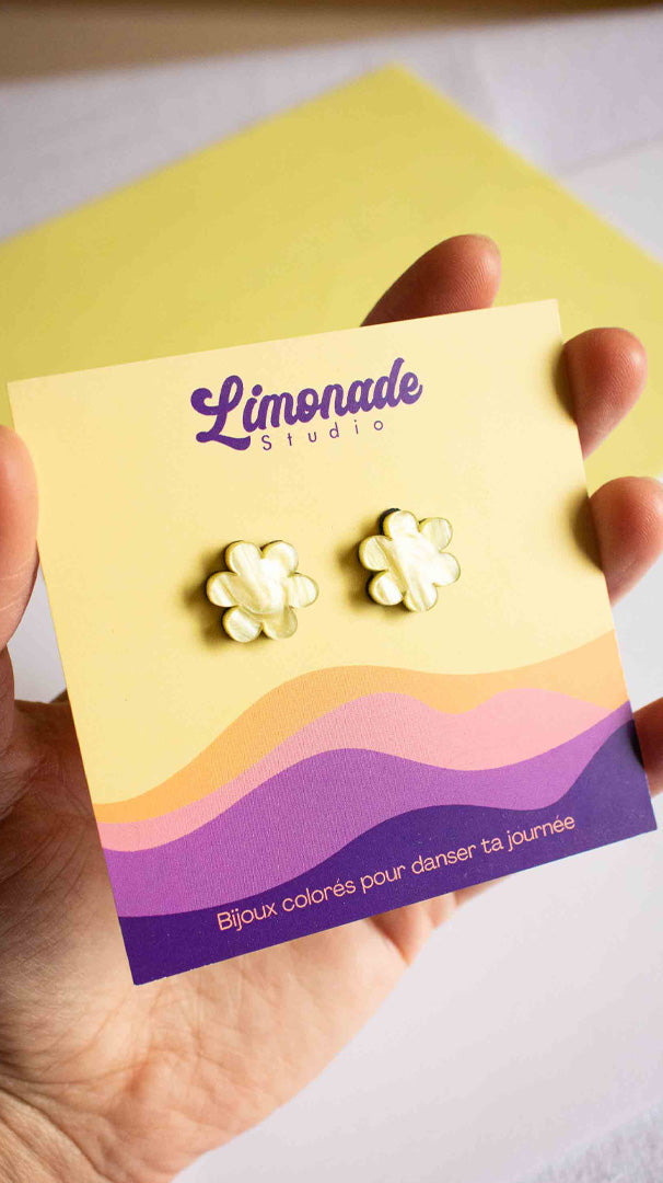 Vidéo des boucles puces jaunes en forme de fleur en acrylique découpé au laser Limonade Studio, portées à l'oreille et présentées dans leur boîte cadeau violette, bijou fantaisie fait main