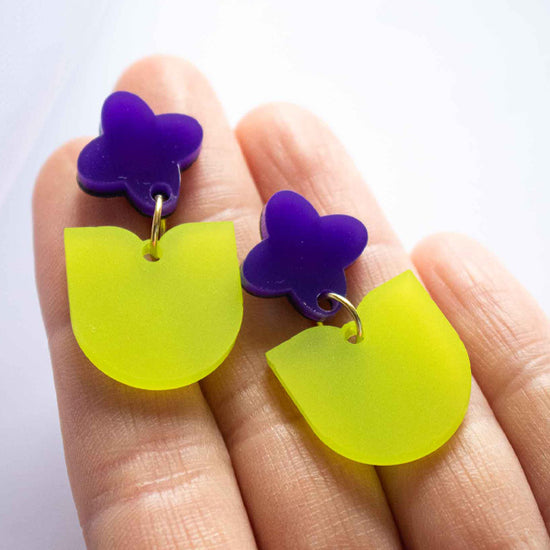 Boucles d'oreilles pendantes fleur violette et feuille verte acrylique dépoli, fait main découpe laser Limonade Studio, portées et présentées avec packaging
